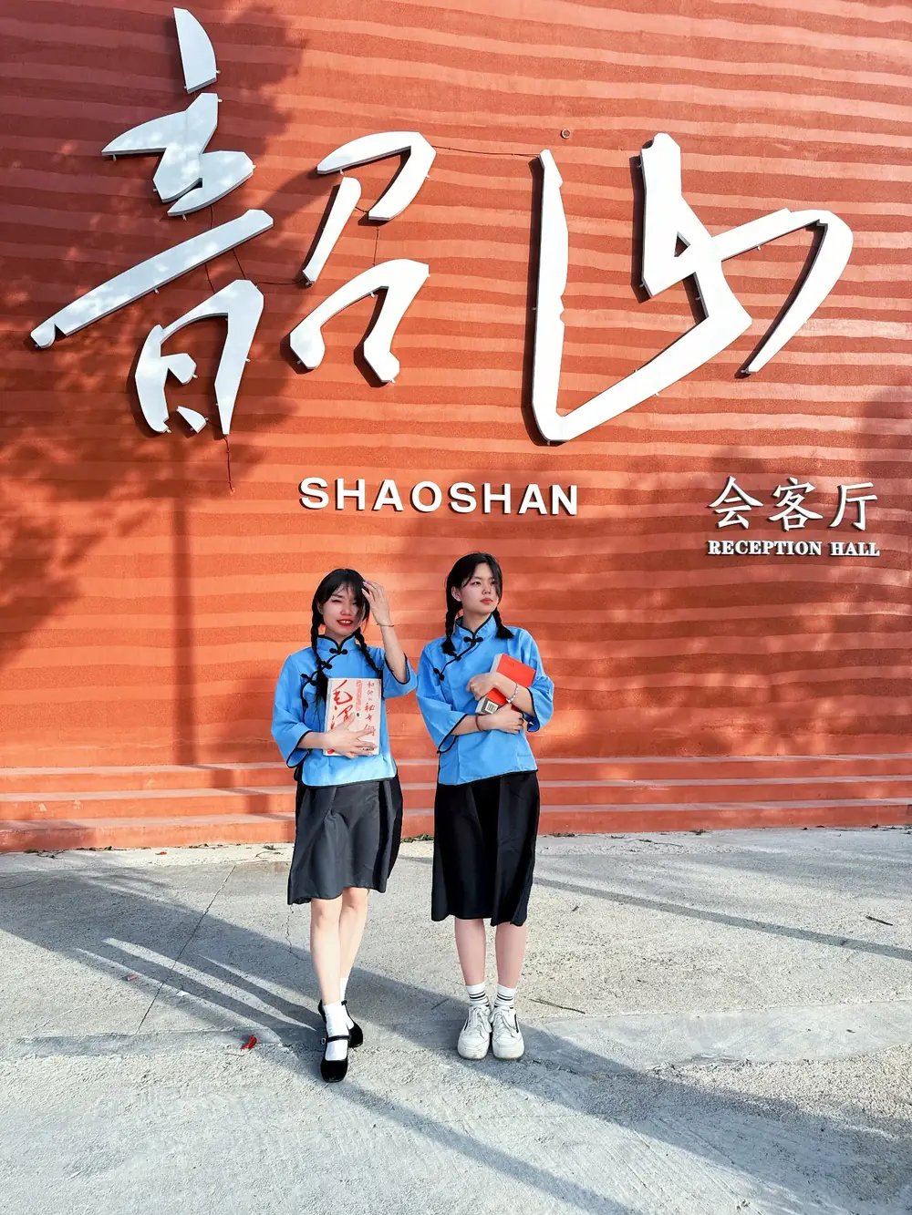 韶山会客厅外墙打卡点：橙红色墙面上的“韶山会客厅 SHAOSHAN RECEPTION HALL”立体大字，游客持书合影